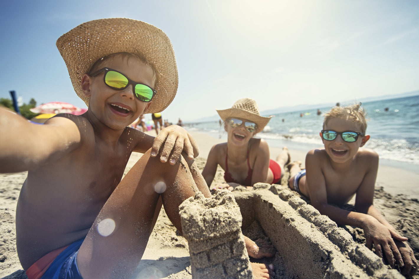mom and two kids smiling with sand castle