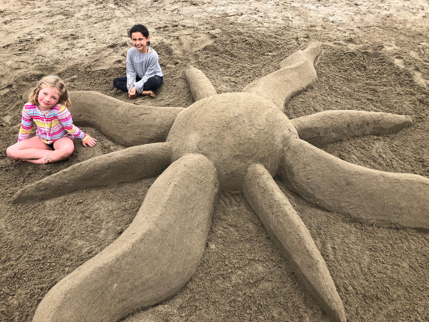 Two girls with an elaborate sand sculpture of the sun created with Pufferfish tools