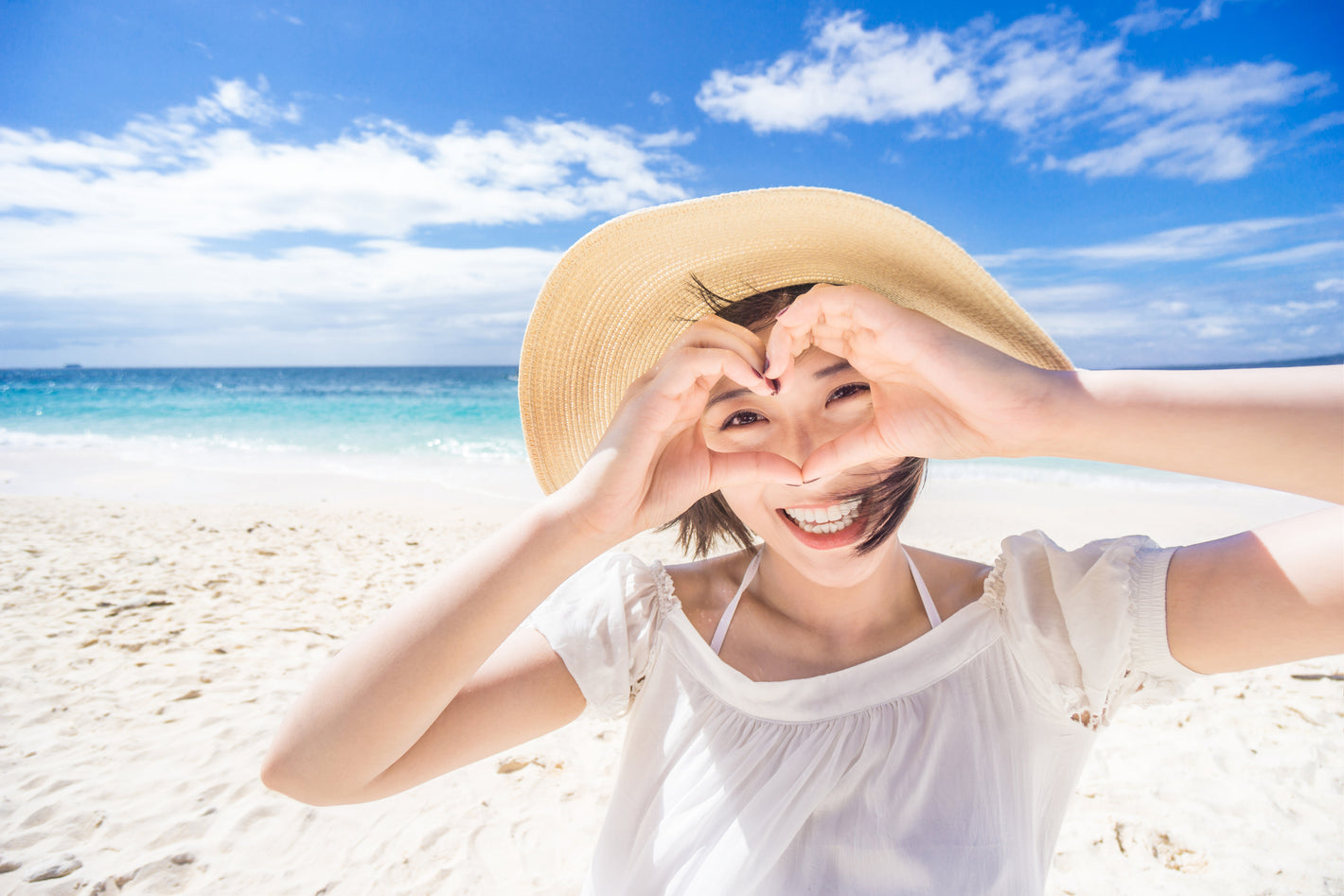 Asian woman at the beach holding up her hands in the shape of a heart