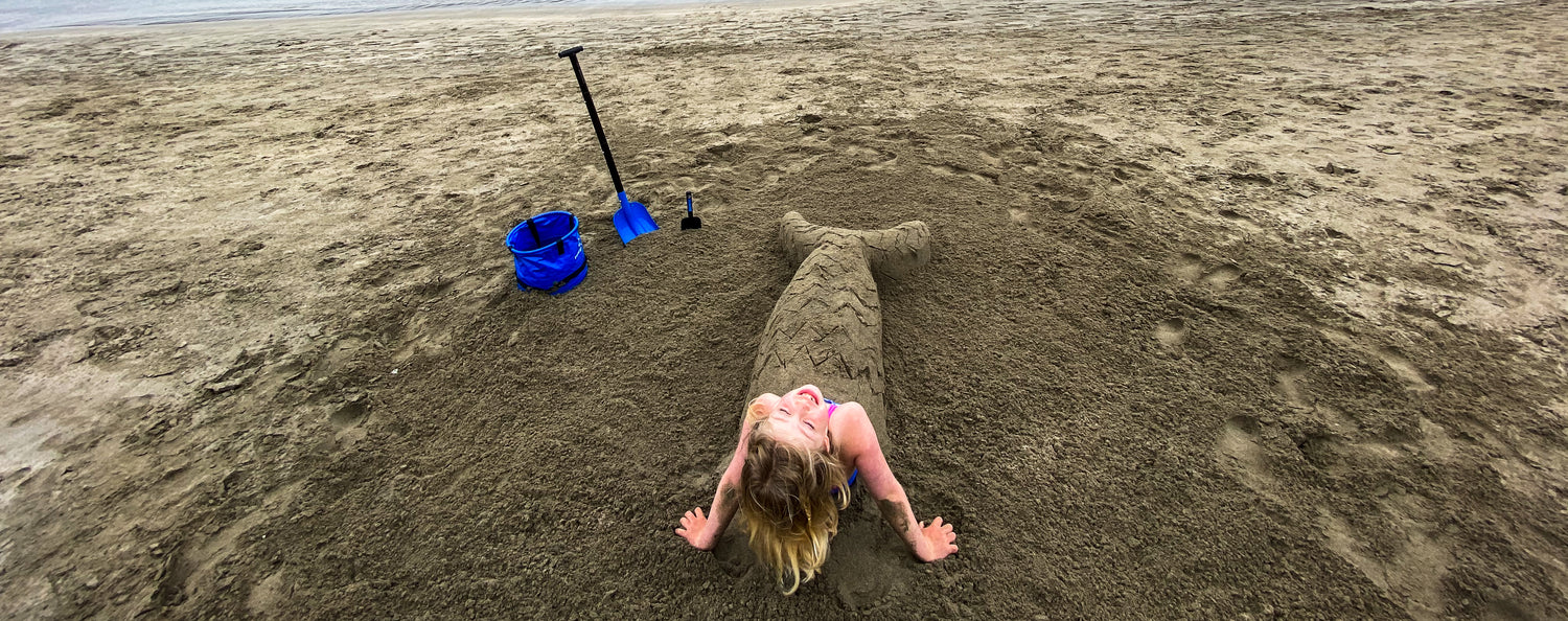 Girl in an elaborate mermaid sandcastle on the beach using Pufferfish sand sculpting tools